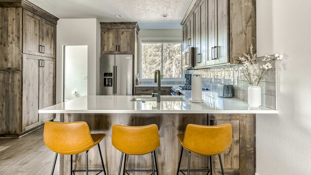 Une cuisine moderne avec des meubles en bois, un îlot central doté de tabourets et une vue sur l’extérieur.