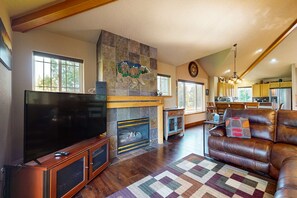 Ein Wohnzimmer mit Kamin, Fernseher, einer Ledersofa und einem Essbereich im Hintergrund.