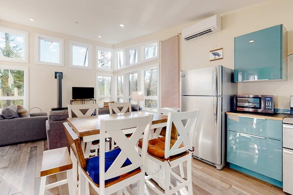 A modern kitchen with a refrigerator, microwave, and dining area with white chairs and a table.