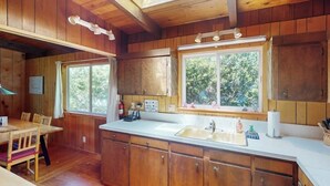A wooden cabin interior with a kitchen area, dining table, and large windows. - Florence oceanfront escape, where cozy meets coastal charm (Florence)