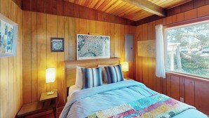 A wooden-paneled room with a bed, two bedside tables, a map on the wall, and a window with a view. - Florence oceanfront escape, where cozy meets coastal charm (Florence)