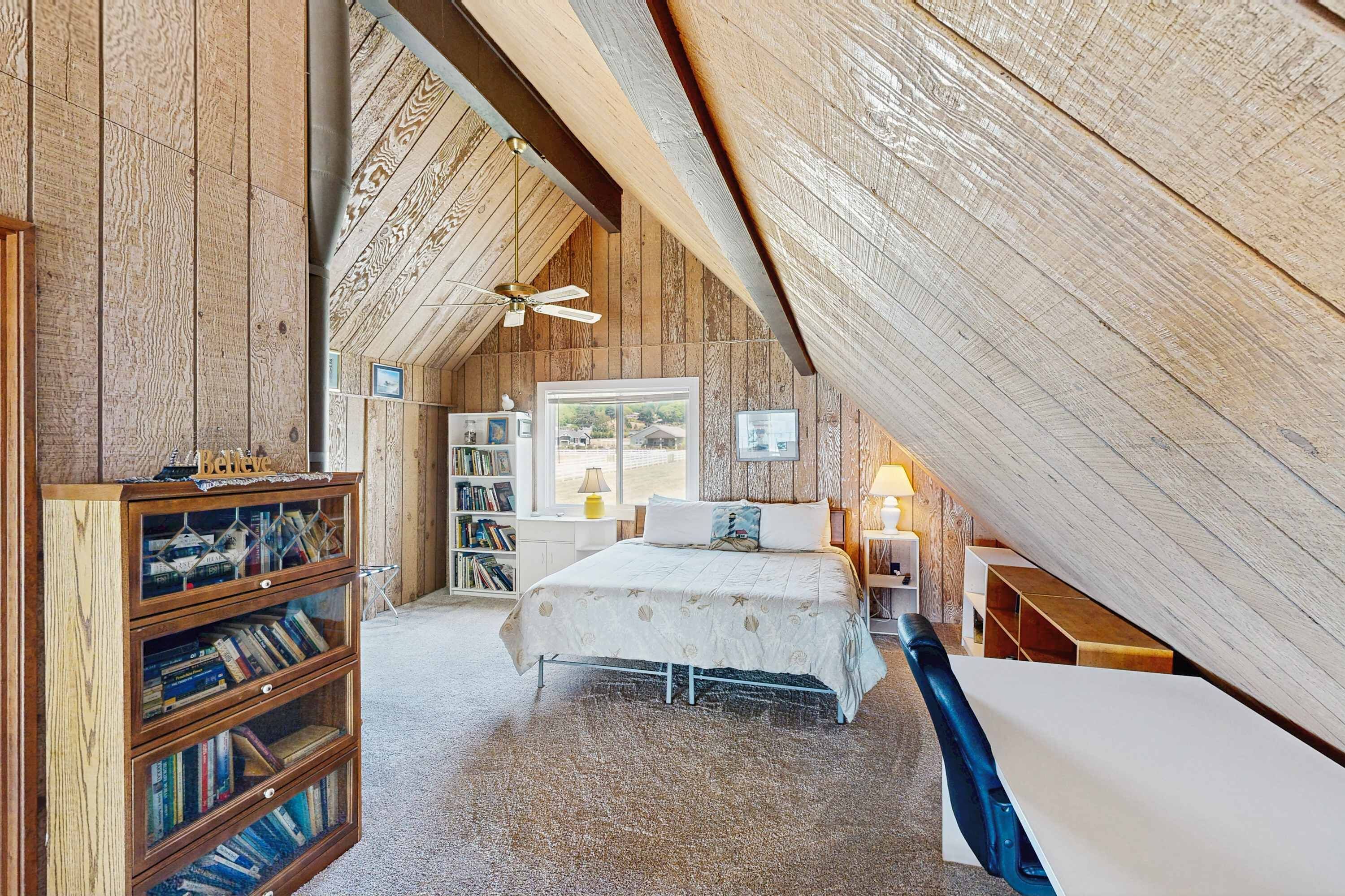 A bedroom with a sloped ceiling, a bed, a bookshelf, a desk, and a chair.