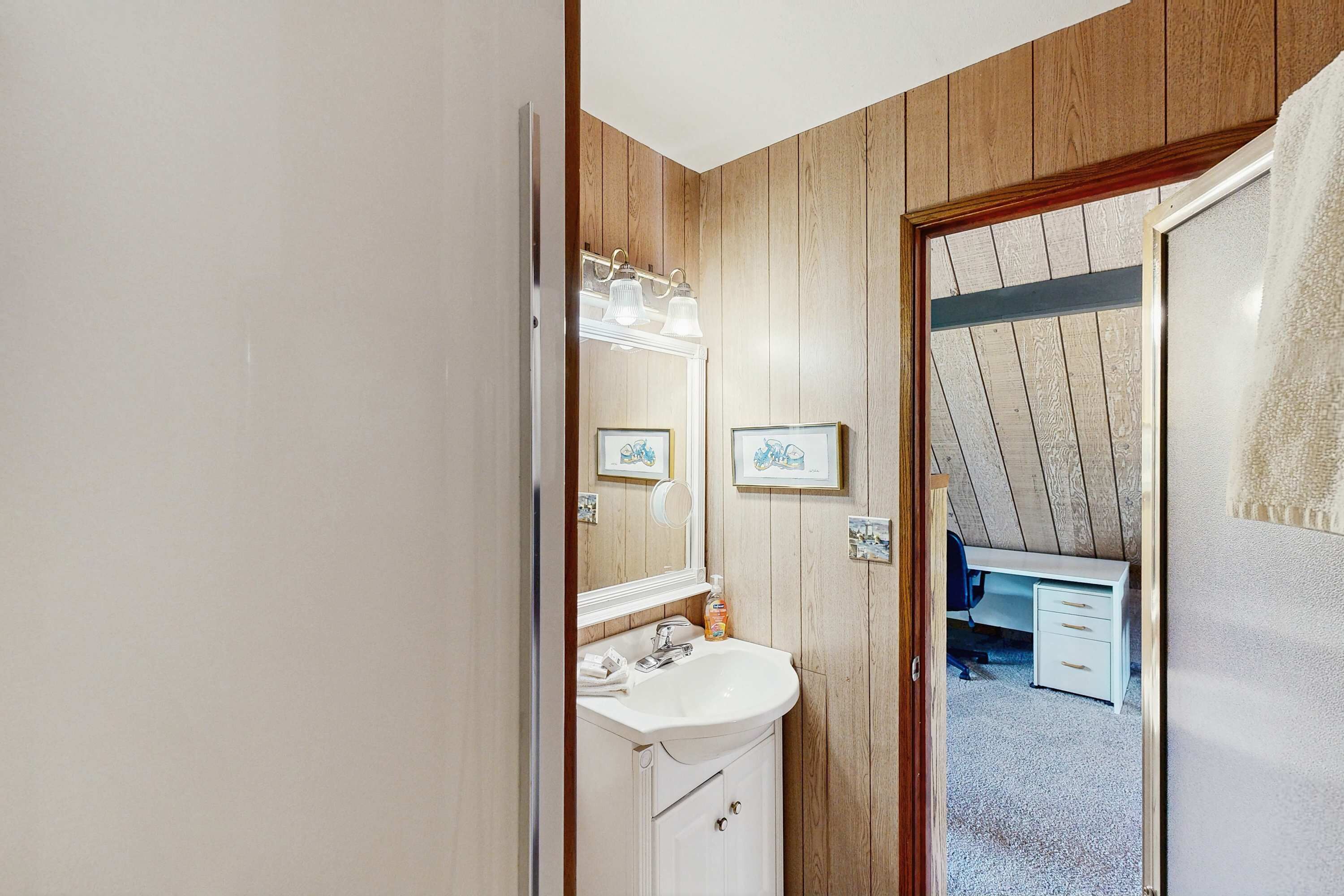 A bathroom with a wooden wall, a white sink, and a mirror.