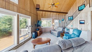 Ein Zimmer mit Holzwandverkleidung, einem Deckenventilator, einem Teleskop, einer Couch, einem Sessel und einer Treppe mit gerahmten Bildern.