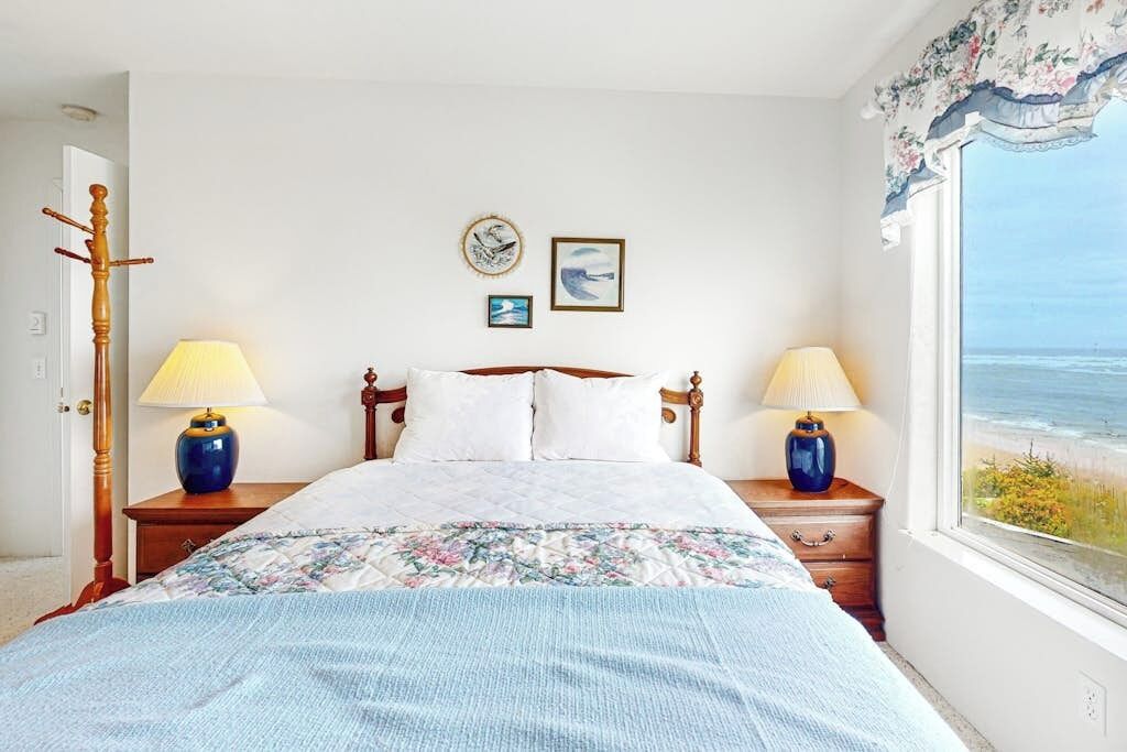 Une chambre à coucher avec un lit, deux lampes de chevet, une fenêtre donnant sur la mer et un porte-manteau.