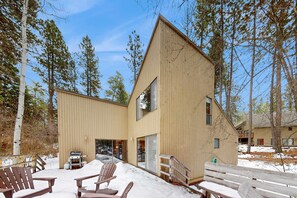 A modern wooden building with a large deck area, outdoor seating, and a snow-covered ground.