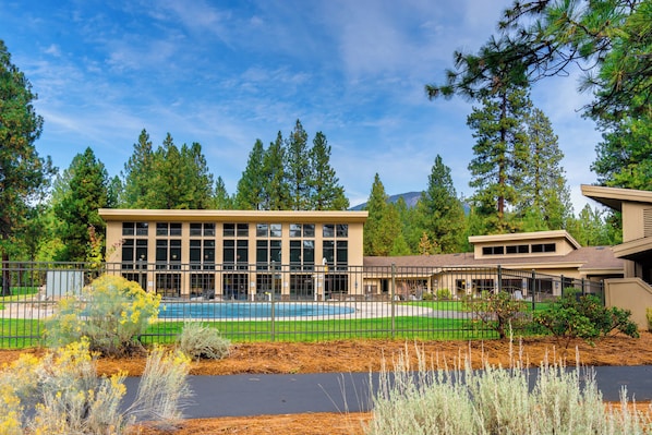 A building with a swimming pool, surrounded by a fence and various trees.