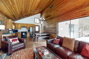 A spacious living area with a wooden ceiling, leather furniture, and a large window offering a view of the outdoors.