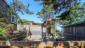 A wooden play structure in a backyard with a wooden fence and a house in the background. - Oceanview Home with Beautiful Deck & Private Playground - Blocks to the Beach (Newport)