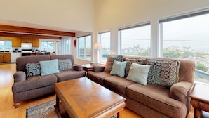 A spacious living area with a large sofa set, a wooden coffee table, and a view of the city through large windows. - Oceanview Home with Beautiful Deck & Private Playground - Blocks to the Beach (Newport)