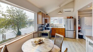 Una cocina moderna con armarios de madera, una mesa de comedor con sillas, vista a un cuerpo de agua y un ventanal grande.