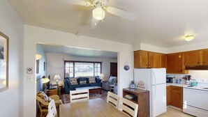 Amplia sala de estar con sofá, mesa de comedor y cocina con armarios de madera y refrigerador.