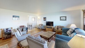 Una sala de estar con sofá, sillones, una mesa de centro, televisor y lámpara.