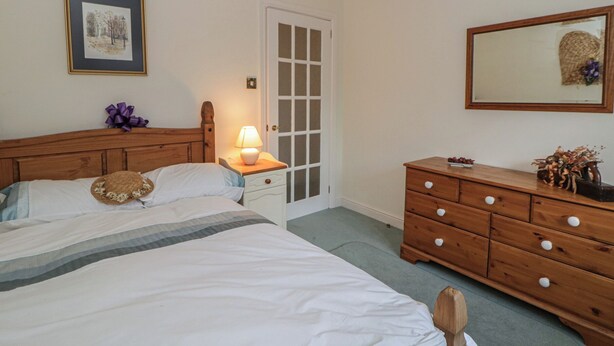A bedroom with a bed, bedside table with a lamp, a dresser, a door, and a framed picture on the wall. - Summerhill (Hereford)