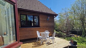 A wooden house with a glass door, a wooden deck, and white outdoor furniture. - Summerhill (Hereford)