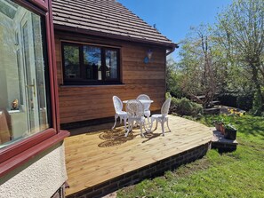 A wooden house with a glass door, a wooden deck, and white outdoor furniture. - Summerhill (Hereford)