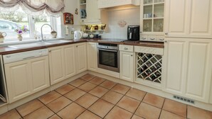 A kitchen with white cabinetry, a dishwasher, an oven, a wine rack, and a window with a curtain. - Summerhill (Hereford)