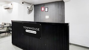Un comptoir d’accueil portant l’inscription « TOWNHOUSE », avec un panneau d’information mis à disposition par l’entreprise, un ventilateur fixé au mur et une caméra de surveillance.