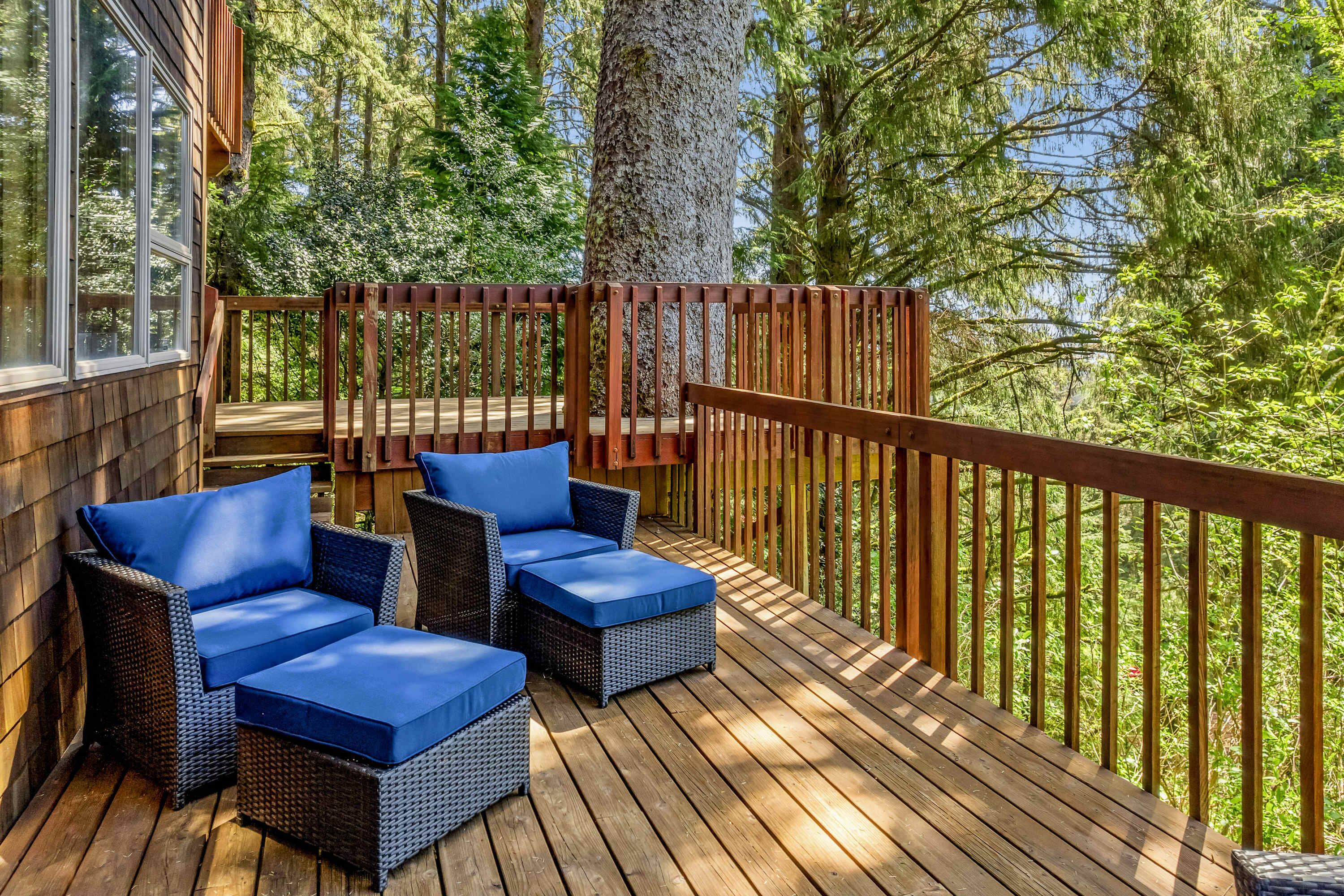 Eine Holzterrasse mit Korbmöbeln und blauen Kissen, umgeben von Bäumen.