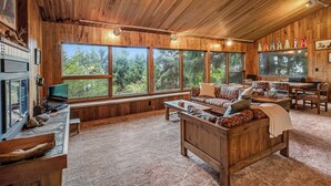 A cozy cabin interior with wooden walls, large windows, a sofa, a table, and a television. - Classic woodland home with gorgeous setting, great deck - 2 dogs OK (Nehalem)