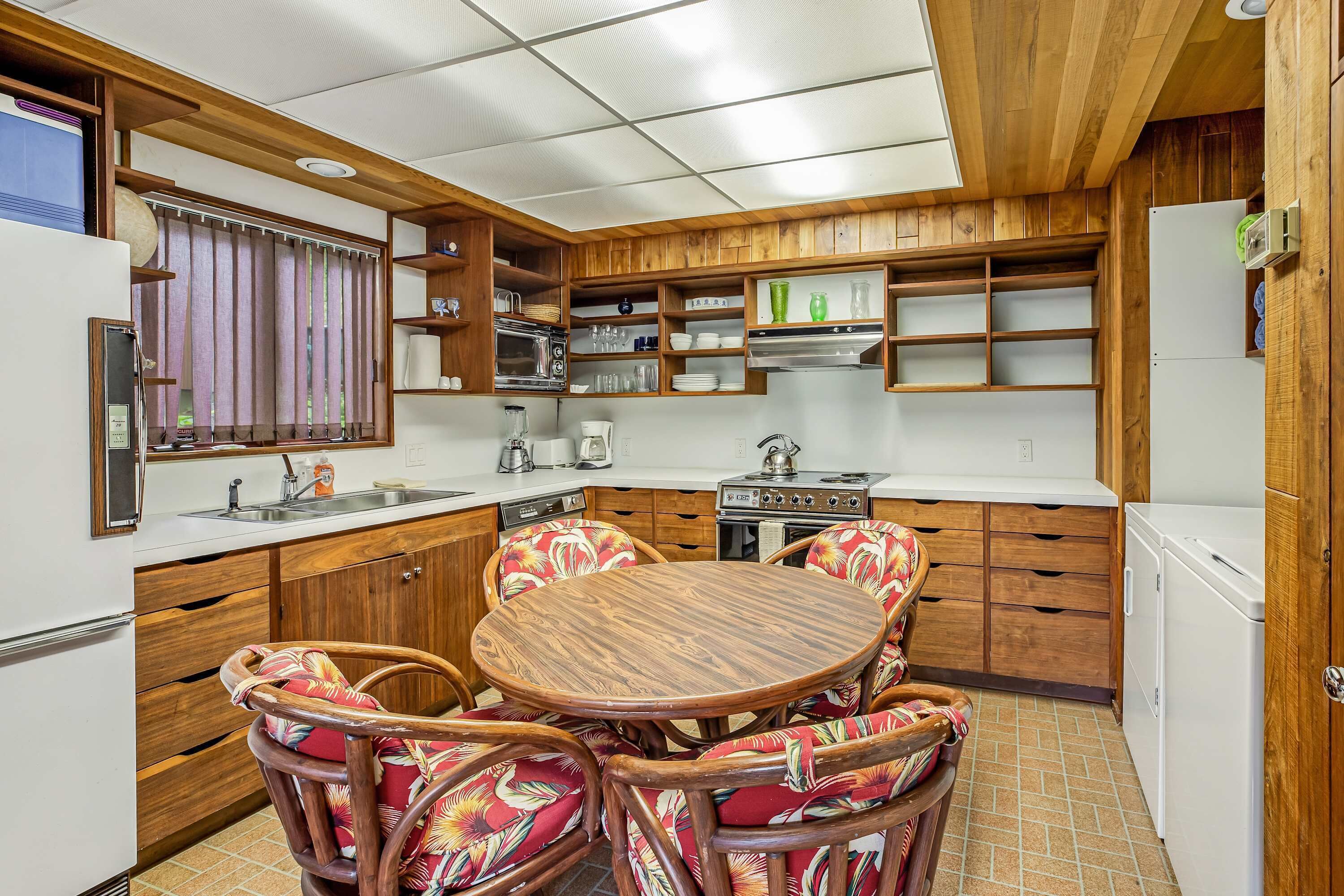 Een kleine keuken met houten keukenkastjes, een eettafel met stoelen en een koelkast.