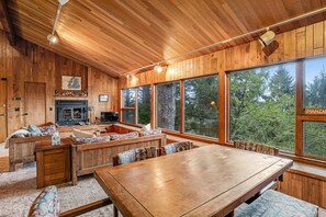 Un intérieur en bois avec une cheminée, de grandes fenêtres et un coin repas.