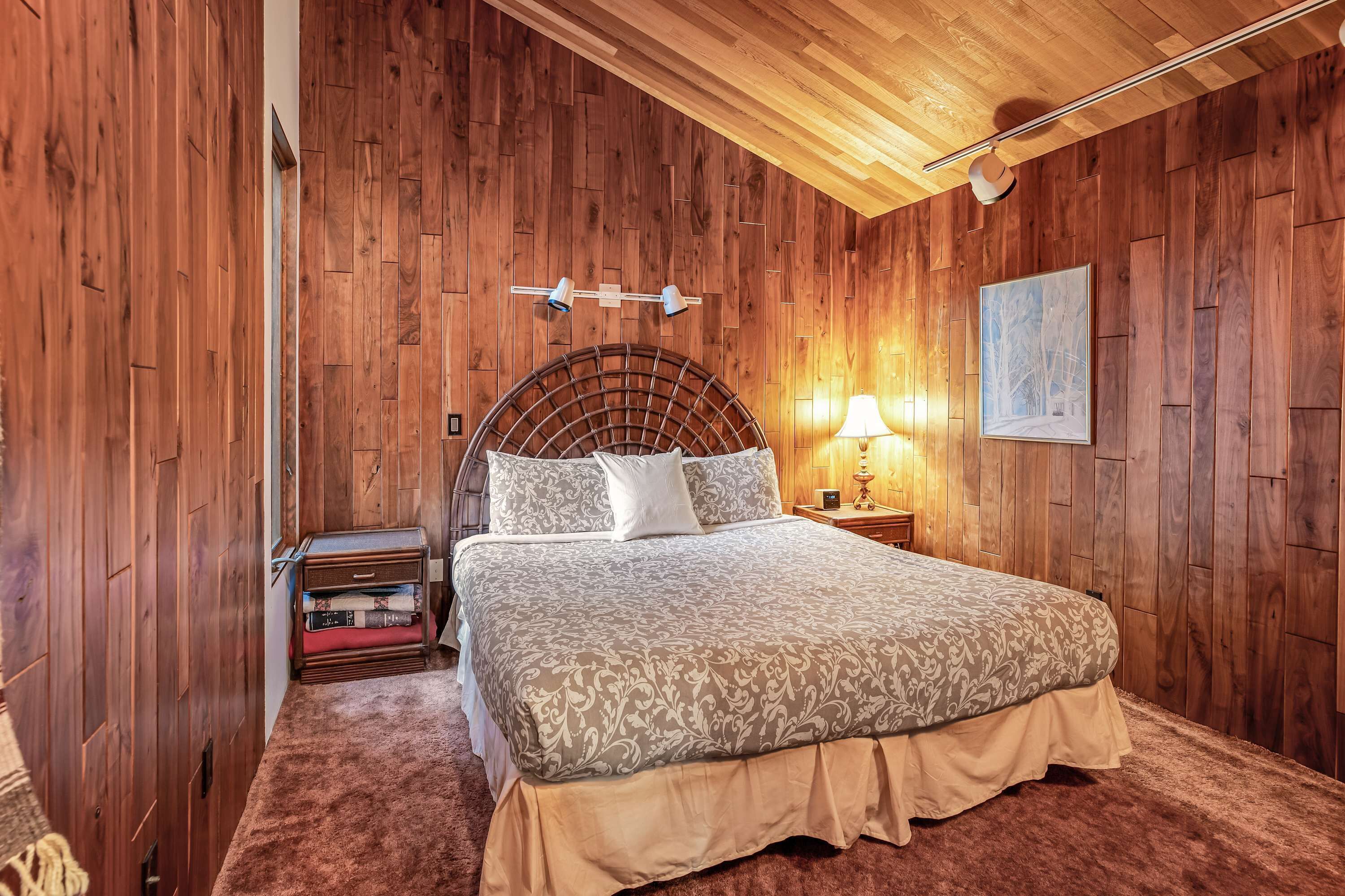 A wooden-paneled room with a bed, a nightstand, and a lamp.