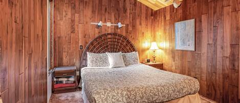 A wooden-paneled room with a bed, a nightstand, and a lamp.