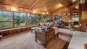 A wooden interior with large windows, a sofa, a dining area, and a kitchen. - Classic woodland home with gorgeous setting, great deck - 2 dogs OK (Nehalem)