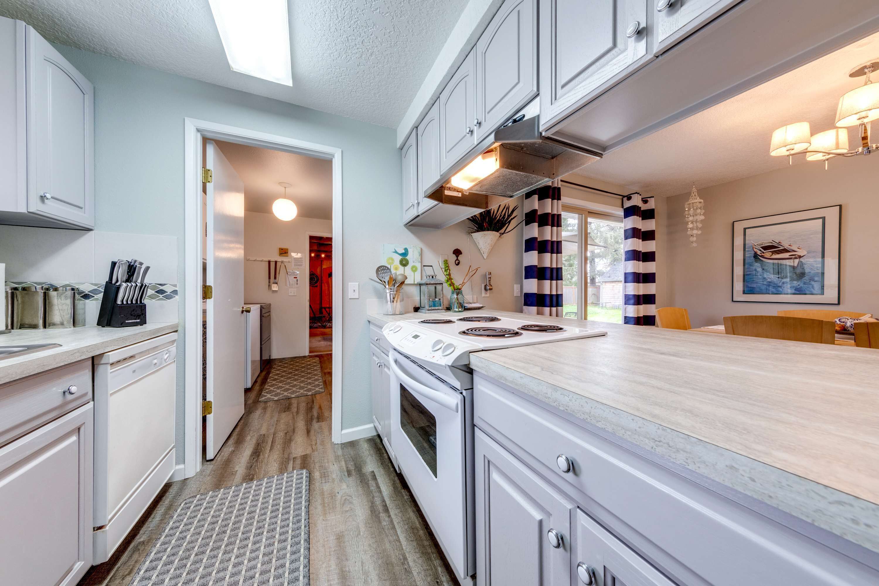 A modern kitchen with white cabinets, a central island, and a dining area with a striped curtain.