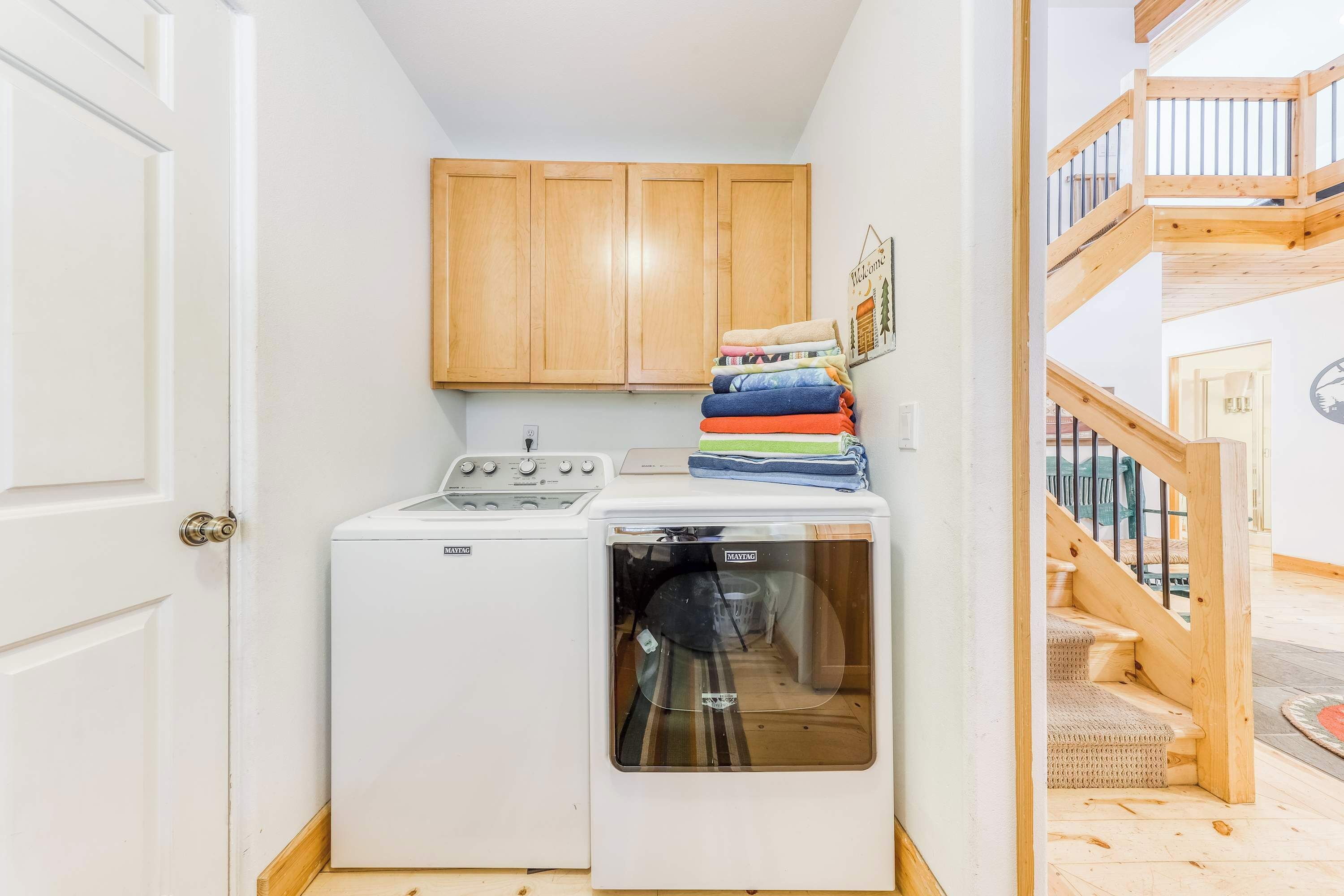 A laundry area with a washing machine and dryer, wooden cabinets, and a staircase.