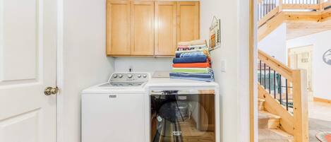 A laundry area with a washing machine and dryer, wooden cabinets, and a staircase.