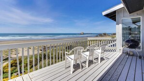 Een houten terras met witte stoelen met uitzicht op een strand.