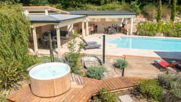 Een achtertuin met een zwembad, een jacuzzi en een overdekt terras.