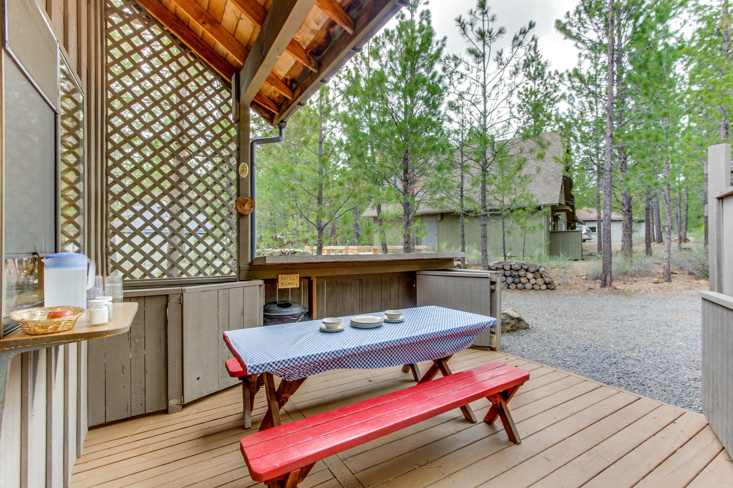 A wooden deck with a picnic table and benches, a grill, and a view of trees.