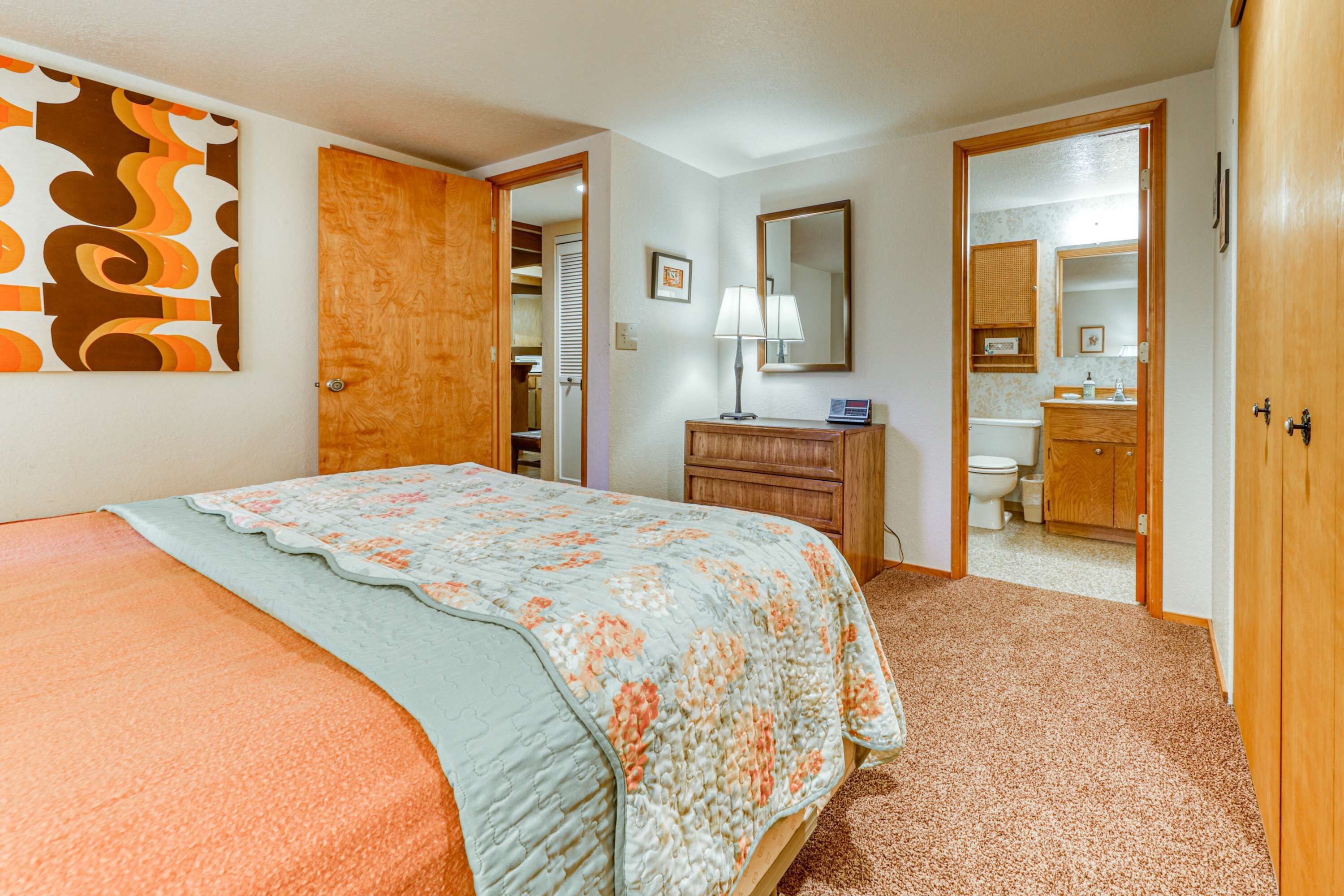 Quarto com cama, penteoudeiro, espelho e banheiro visível por uma porta aberta.