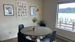 A room with a round table, four chairs, a potted plant, and a window with a view of a body of water.