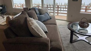 A living room with a large window overlooking a lake, a brown sofa, and a glass coffee table.