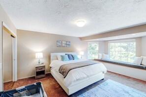 A bedroom with a bed, nightstand, lamp, window seat, and artwork on the wall.