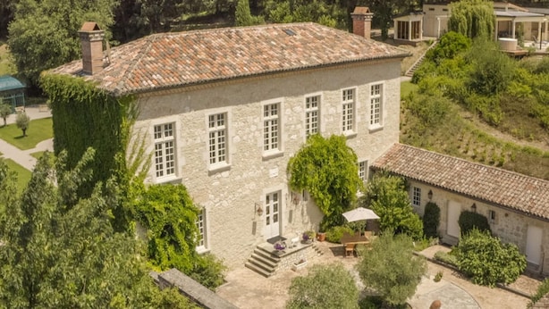 Ein Steinhaus mit mehreren Fenstern, einem Innenhof und umliegender Bepflanzung.