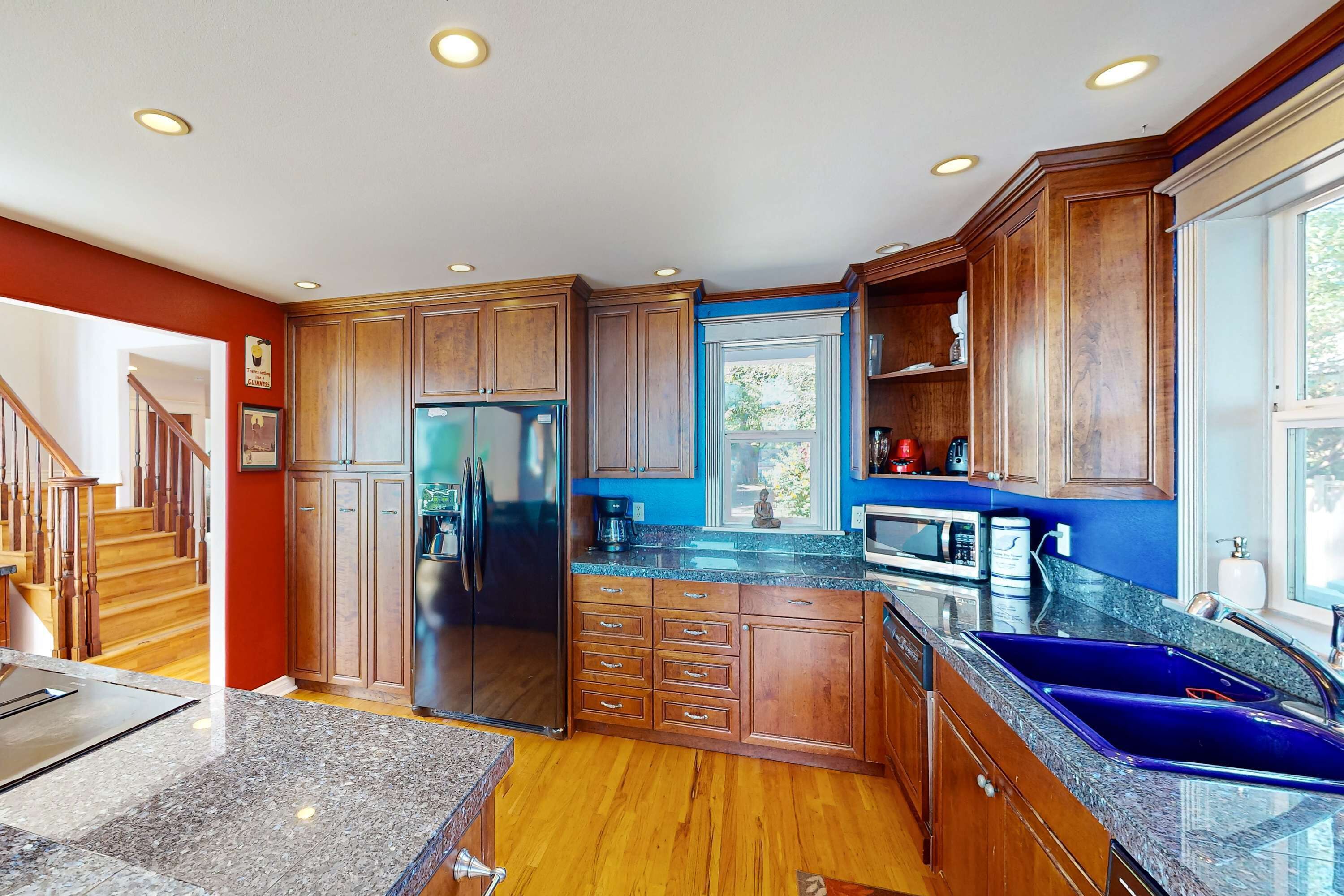 Una cocina con armarios de madera, encimeras de granito, refrigerador de acero inoxidable y un lavamanos azul.
