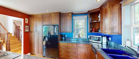 Una cocina con armarios de madera, encimeras de granito, refrigerador de acero inoxidable y un lavamanos azul.