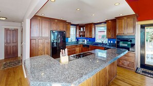 A modern kitchen with granite countertops, wooden cabinets, stainless steel appliances, and a large island. - Bay & Harbor View Home with High-Speed WiFi, Private Washer/Dryer, & Board Games (Newport)