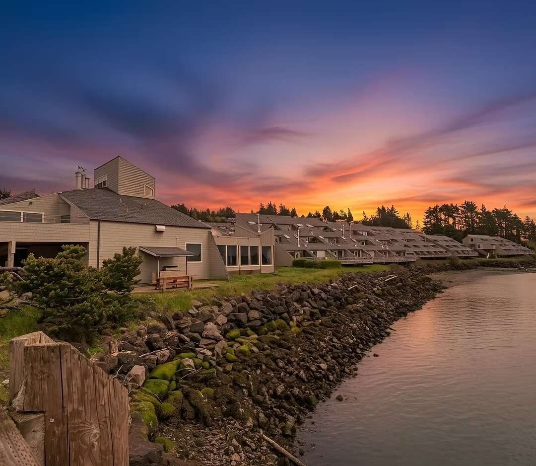 Een pand aan het water met meerdere huizen, een houten steiger en een rotsachtige oever.