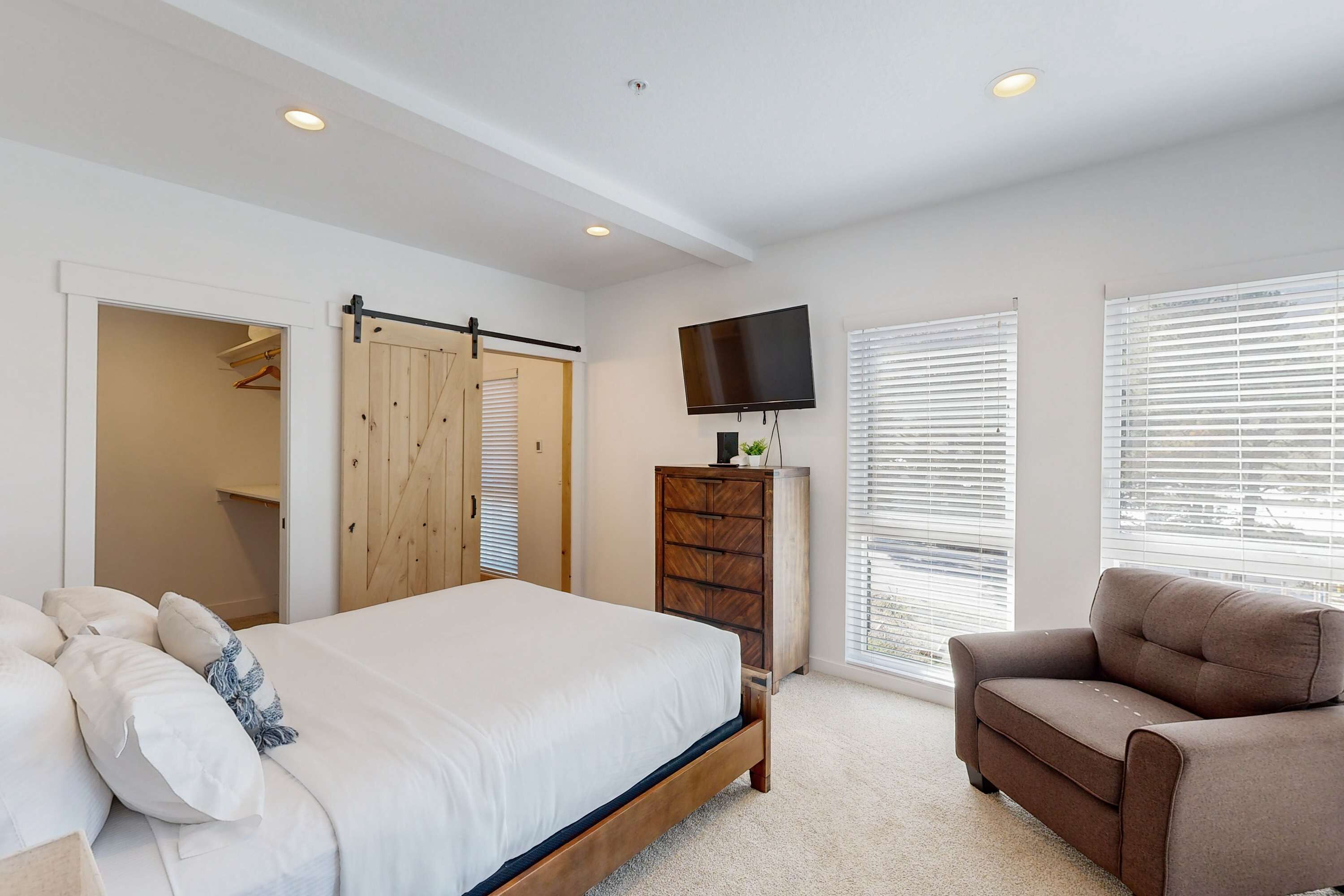 Un dormitorio con cama, cómoda, televisor y ventana con persianas.