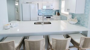 Een moderne keuken met witte kastjes, een centraal eiland met een spoelbak en vier rieten stoelen.