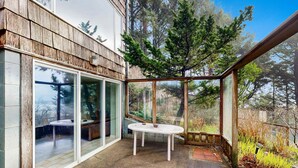 Veranda vetrata con tavolo e sedie, circondata da rivestimenti in legno e affaccio su alberi.