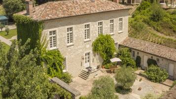 A stone building with multiple windows, a courtyard, and surrounding greenery.