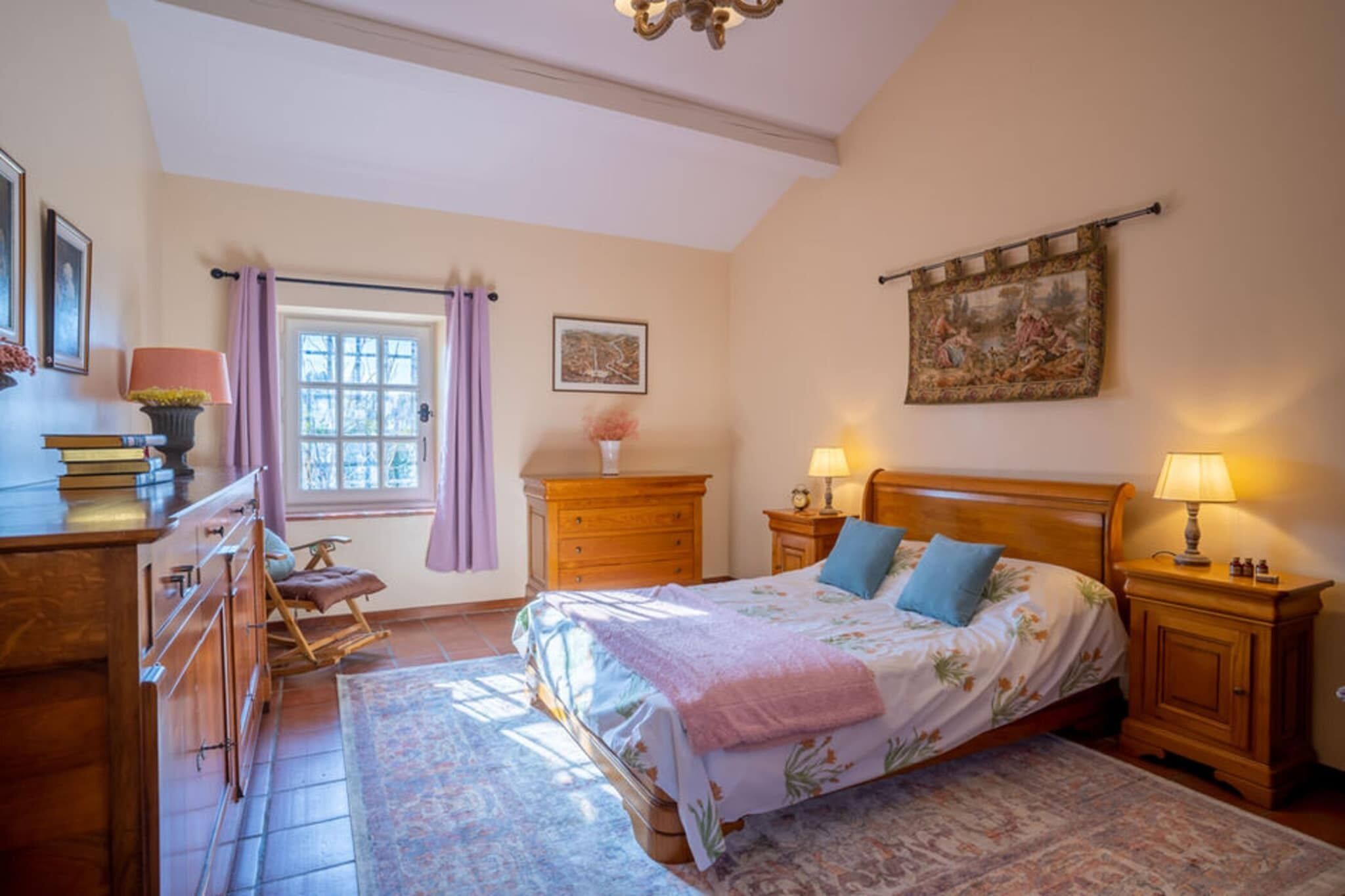 A bedroom with a bed, bedside tables, a dresser, a window with curtains, and a painting on the wall.