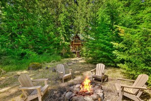 Ein bewaldetes Gebiet mit Lagerfeuerstelle und Adirondack-Stühlen.